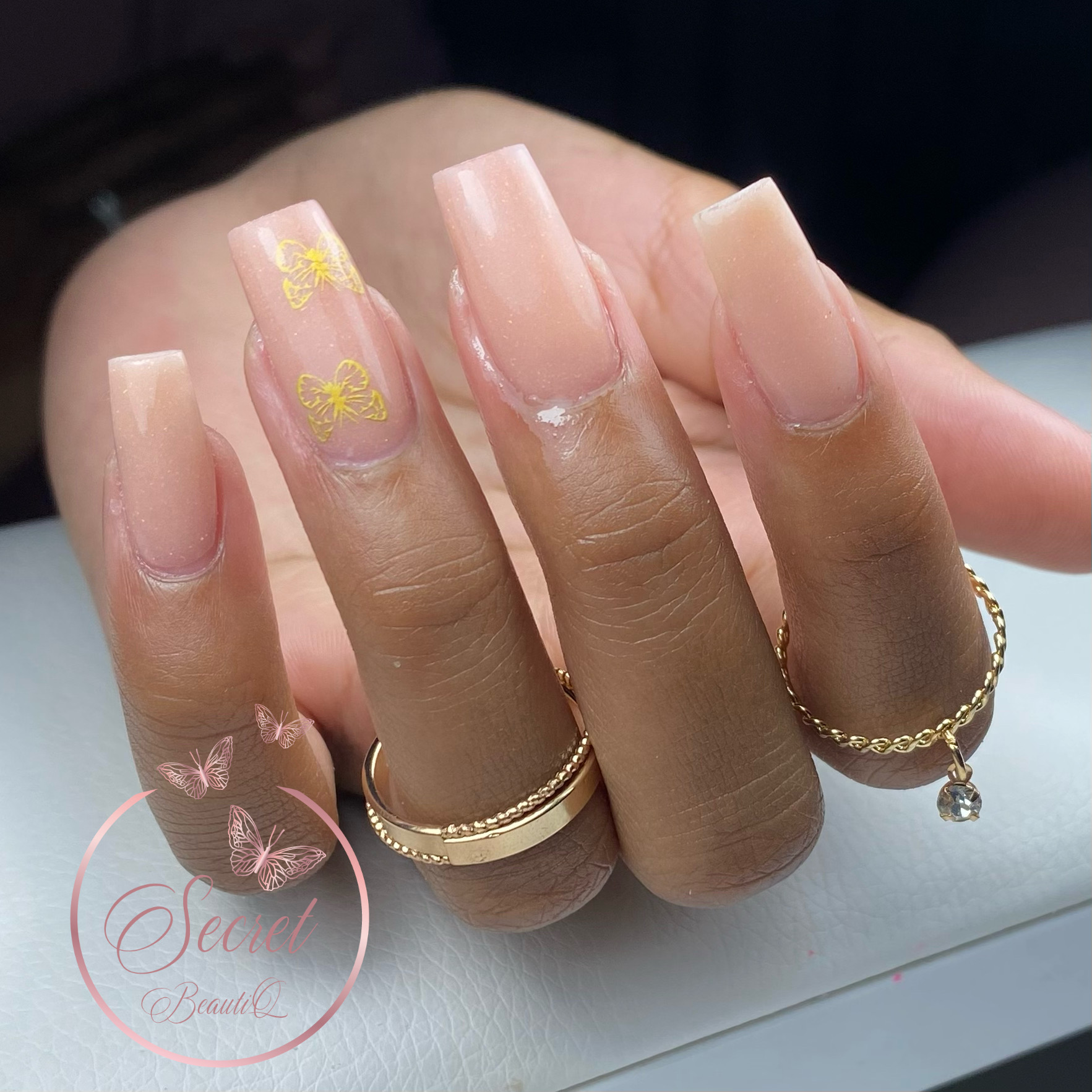 Nude kunstnagels met gouden vlinders op een hand met ringen