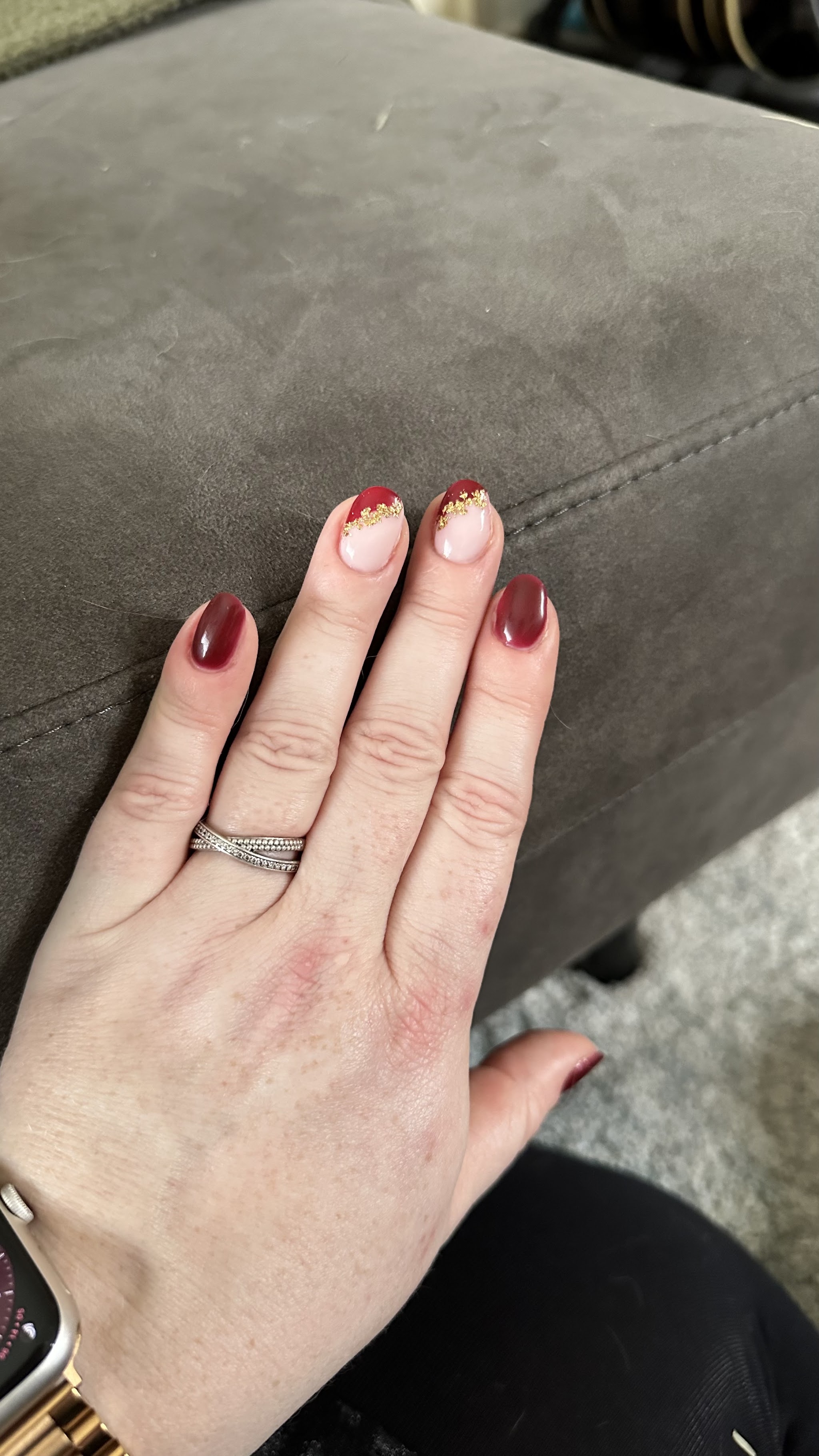 Rode nagels met gouden tips op een hand, op een grijze bank