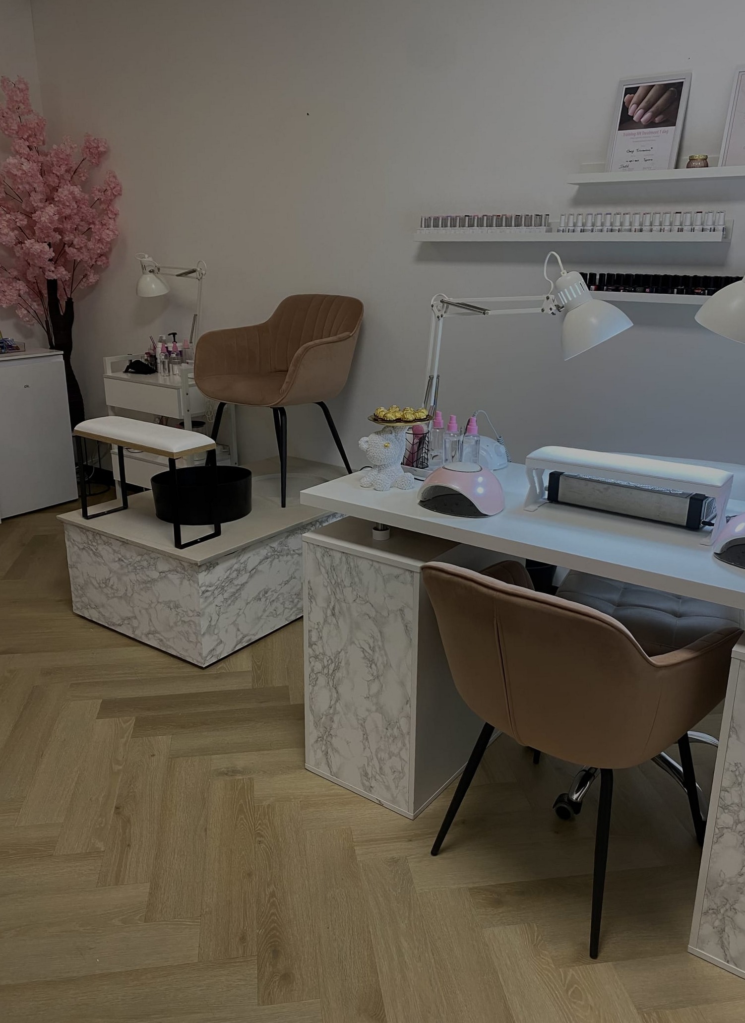 De studio van Secret BeautiQ: marmeren werktafel met nagellampen, cognackleurige stoelen, een roze bloesemboom en een visgraatvloer